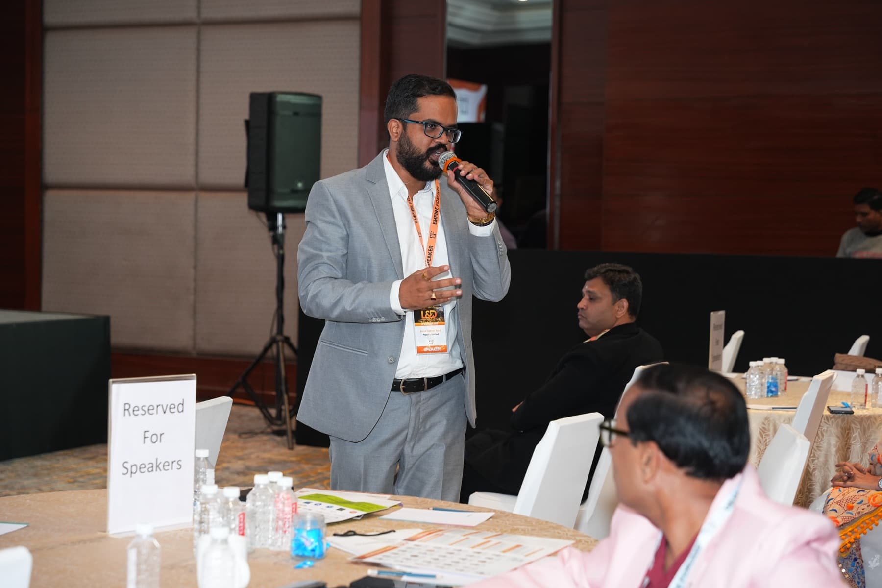 Amit Kumar Soni in a grey suit speaking into a microphone at a conference table.