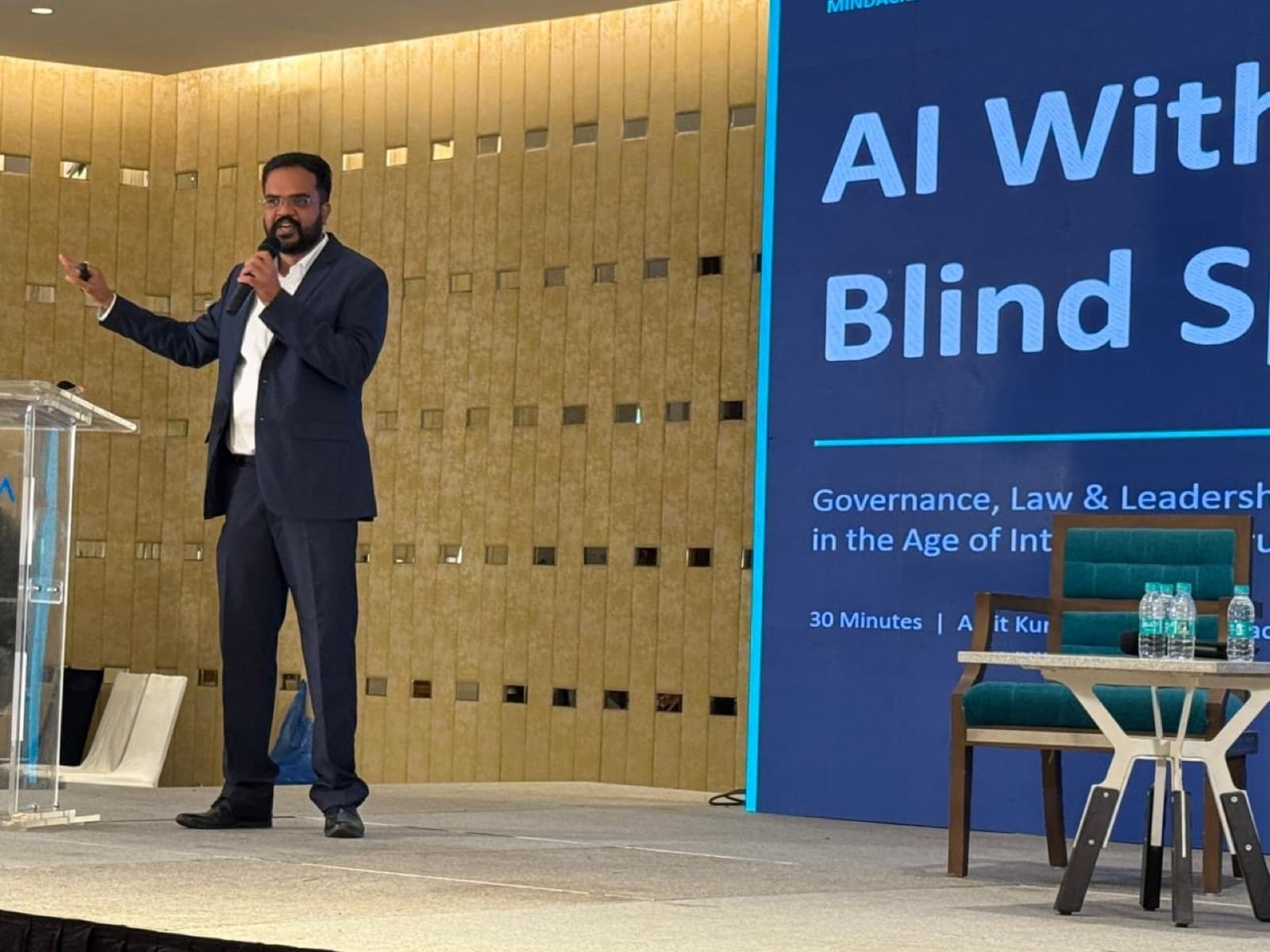 Amit Kumar Soni speaking from a lectern beside a large screen about AI governance.
